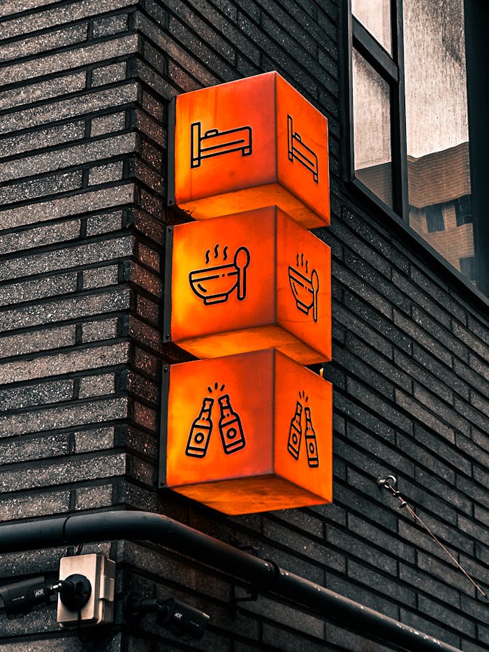 Illuminated cube signs on a brick wall in Seoul showing bed, food, and drink symbols.
